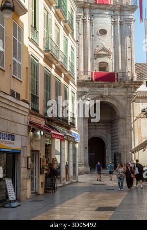 Die Leute laufen durch eine enge Straße mit der Kirche San Juan Bautista - Iglesia de San Juan, im Hintergrund im alten Zentrum von Malaga. Stockfoto
