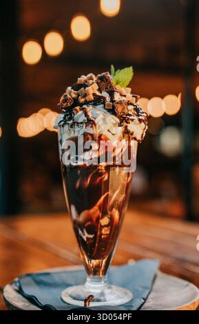 Ein Glas Schokoladeneis mit Schlagsahne und Schokoladensoße darauf. Das Bild hat eine warme und einladende Stimmung, da es ein köstliches Dessert zeigt Stockfoto