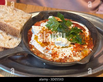 Shakshuka mit Brot, serviert in einer Eisenpfanne. Mediterraner Geschmack, Frische und hausgemachter Komfort im Café-Frühstücksgericht. Stockfoto