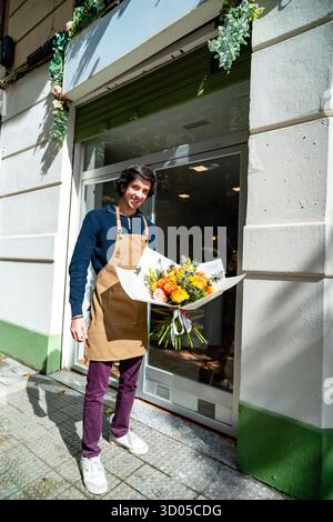 Junger Mann mit Schürze, der einen frischen Blumenstrauß vor seinem Laden hält Stockfoto