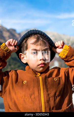 Vertikales Porträt eines Reisenden Jungen, der eine Kaltwetterkappe trägt, während eines Wanderweges im Nationalpark, umgeben von der Natur, vor dem klaren Wasser Stockfoto