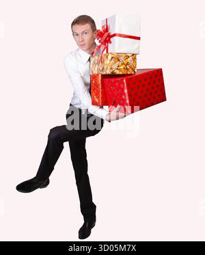 Ein Mann in Hemd und Krawatte hält mehrere farbenfrohe Geschenkboxen, die Feierlichkeiten, Feiertage oder Großzügigkeit repräsentieren. Stockfoto