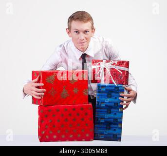 Ein Mann in Hemd und Krawatte hält mehrere farbenfrohe Geschenkboxen, die Feierlichkeiten, Feiertage oder Großzügigkeit repräsentieren. Stockfoto