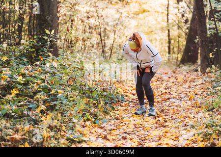 Läuferin sportlich gekleidet im herbstlichen Park, vor Schmerzen gekrümmt, beim morgendlichen Joggen im gelben Herbstpark akuten Magenkrämpfe Schmerzen spürt. Stockfoto