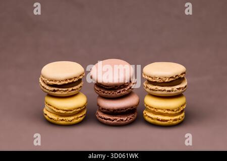 Verschiedene Macarons in Braun- und Gelbtönen, gestapelt auf braunem Hintergrund. Die Komposition bietet warme Farbharmonie und geeigneten Kopierraum Stockfoto