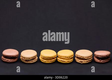 Fünf verschiedene Macarons in horizontaler Reihe auf dunklem Hintergrund. Das elegante Arrangement bietet einen modernen, minimalistischen Stil, ideal für Bäckereien, die mit einem Branding versehen werden Stockfoto