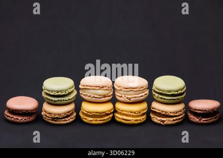 Eine Gruppe gemischter Pastell-Macarons, die in einer sanften Linie auf dunklem Hintergrund angeordnet sind. Die elegante Lebensmittelkomposition eignet sich perfekt für Süßwarenwerbung Stockfoto