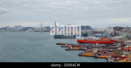 BUSAN, SÜDKOREA - 9. OKTOBER 2025 - Busan Hafen mit verschiedenen Schiffen an einer großen Werft und einer Skyline der Stadt Stockfoto