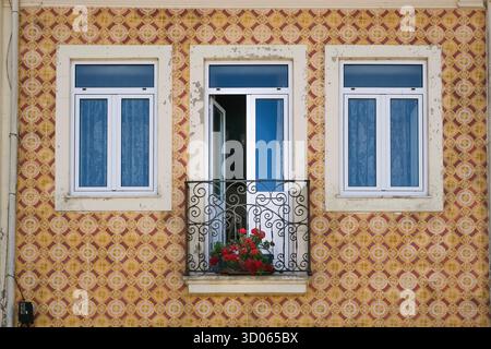 Farbenfrohe traditionelle portugiesische Fassade mit gekachelten Wänden, drei Fenstern und einem kleinen Balkon mit roten Blumen, die klassische Architektur und zeigen Stockfoto
