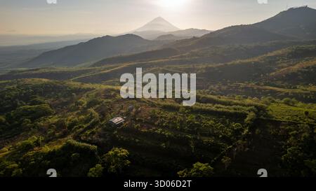Atemberaubende Luftaufnahmen machen eine riesige, trübe Berglandschaft in Flores bei Sonnenaufgang. Goldenes Licht erleuchtet sanfte Hügel mit einer kleinen Hütte, die führt Stockfoto