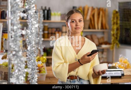 Die junge Frau im Laden wählt Hüttenkäse, scannt das Produktetikett mit dem Telefon Stockfoto