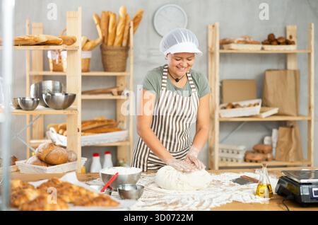 Frau arbeitet in der Bäckerei als Bäckerin, knetet Teig, arbeitet mit Mehl. Stockfoto