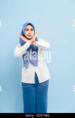 Porträt eines ernsthaften asiatischen muslimischen Arztes oder einer Krankenschwester mit „Stop“- oder „No“-Geste mit gekreuzten Armen, isoliert auf blauem Hintergrund. Stockfoto