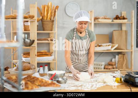 Frau arbeitet in der Bäckerei als Bäckerin, knetet Teig, arbeitet mit Mehl. Stockfoto