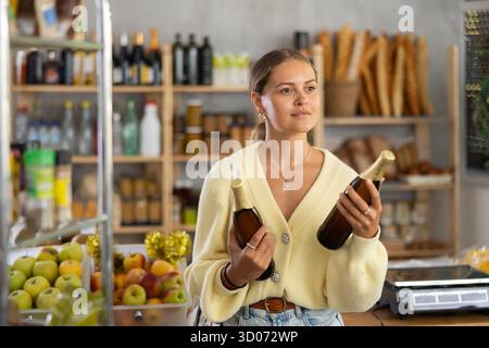 Die Käuferin untersucht Bierflaschen, wählt den richtigen Hersteller, nimmt verschiedene Flaschen aus dem Regal. Stockfoto