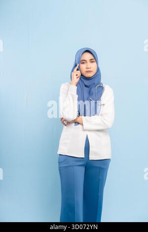 Porträt eines besorgten asiatischen muslimischen Arztes oder einer Krankenschwester, der tief denkt, isoliert einen blauen Hintergrund. Stockfoto