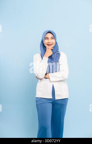 Porträt eines besorgten asiatischen muslimischen Arztes oder einer Krankenschwester, der tief denkt, isoliert einen blauen Hintergrund. Stockfoto