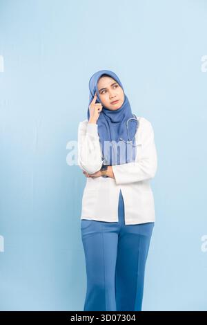 Porträt eines besorgten asiatischen muslimischen Arztes oder einer Krankenschwester, der tief denkt, isoliert einen blauen Hintergrund. Stockfoto