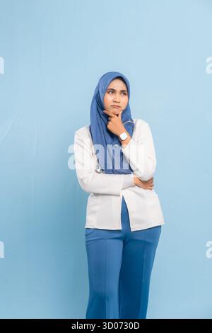 Porträt eines besorgten asiatischen muslimischen Arztes oder einer Krankenschwester, der tief denkt, isoliert einen blauen Hintergrund. Stockfoto