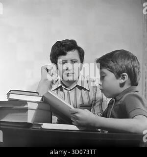Ein sowjetischer Vater, ein Maschinist, beobachtet aufmerksam, wie sein Sohn in Sloviansk, 1970er-1980er, ein Buch liest Dieses Archivfoto aus der UdSSR, Ukrainische SSR, ist ein intimes Porträt von Vater und Sohn. Der Mann in einem gestreiften Hemd hält eine Zigarette, während er den Jungen beobachtet, der sich auf sein Studium konzentriert. Ein großer Stapel Bücher sitzt auf dem polierten Tisch. Dieses Bild zeigt eine Szene des sowjetischen Alltags, der Vaterschaft, der Familienwerte und der Bildung zu Hause. Ein nostalgisches Dokument des friedlichen Lebens im Donbass vor dem Krieg. Stockfoto