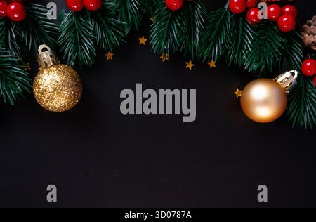 Elegante goldene Weihnachtsschmuck und Tannenzweige bilden festlichen Rahmen auf Schwarz. Perfekt für hochwertige Designs im Winter. Stockfoto