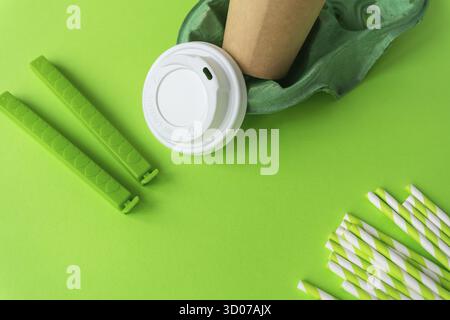 Dieses Bild zeigt eine umweltfreundliche Einweg-Kaffeetasse mit grünen Silikonbändern und Papierhalmen vor einem leuchtend grünen Hintergrund. Die Produkte Stockfoto