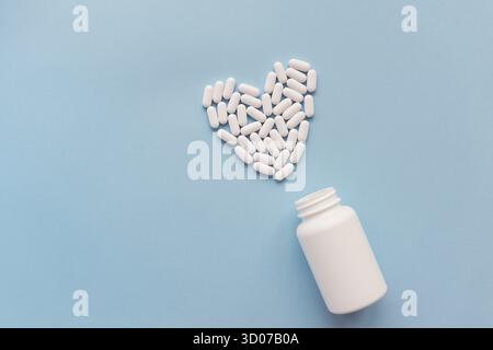 Weiße Pillen in Herzform und ein weißes Glas auf blauem Hintergrund. Pillen für die Gesundheit des Herzens. Das Konzept der Medizin und Gesundheitsversorgung Stockfoto