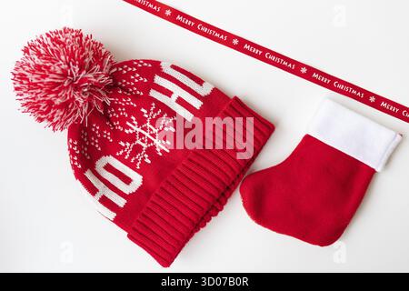 Rotes Band mit Aufschrift Frohe Weihnachten mit rotem Hut, Fäustlingen und roter Socke auf weißem Tisch. Das Konzept der Neujahrsfeier und Stockfoto