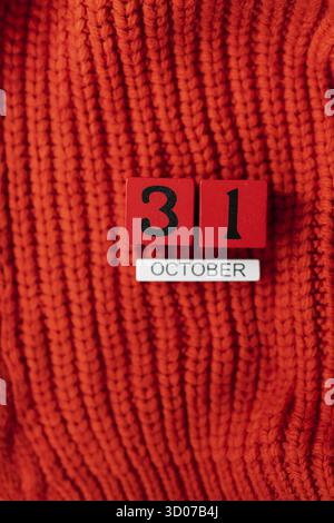 Holzwürfelkalender zeigt am 31. Oktober Halloween isoliert auf rotem Hintergrund rot gestrickter Pullover Stockfoto