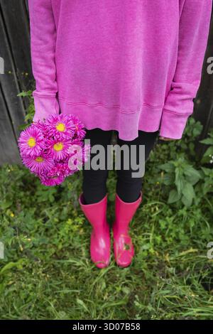 Eine Frau in rosa Stiefeln und einem rosa Pullover hält einen schönen rosa Blumenstrauß in ihren Händen. Das Mädchen steht auf der Straße Stockfoto