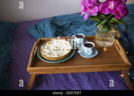 Frühstück im Bett. Wunderschöne Pfingstrosen, leckeren Käsekuchen und zwei Tassen Kaffee auf einer hölzernen Fach Stockfoto
