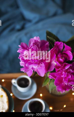 Frühstück im Bett. Schönes Licht aus den Schaufensterpeionen, Käsekuchen und zwei Tassen Kaffee auf einem Holztablett. Nahaufnahme Stockfoto