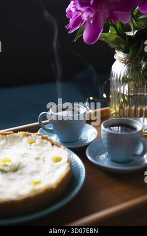 Frühstück im Bett. Wunderschöne Pfingstrosen, leckeren Käsekuchen und zwei Tassen Kaffee auf einer hölzernen Fach Stockfoto