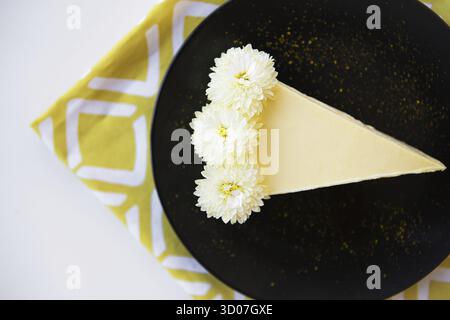 Cremiger Käsekuchen mit weißen Blüten auf einer gelben Serviette Stockfoto