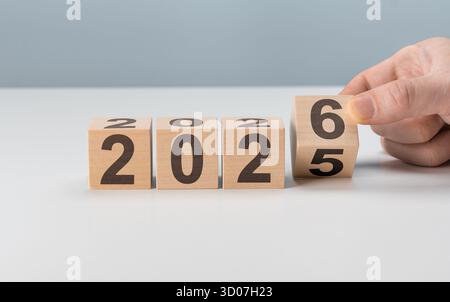 Die Hand des Mannes verwandelt einen Holzwürfel von 2025 auf 2026. Symbolisiert den Beginn des neuen Jahres, bevorstehende Veränderungen und zukünftige Chancen Stockfoto