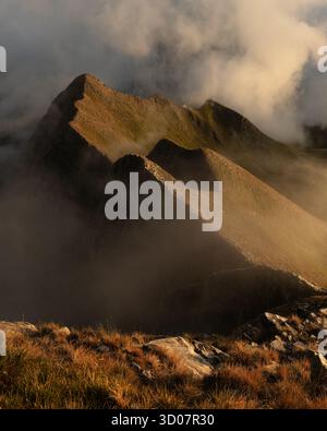 Der Blick auf die zerklüfteten Berggipfel erhebt sich durch ein Meer aus wirbelnden Wolken, die in das warme Licht des Sonnenlichts getaucht sind, und schafft eine dramatische Landschaft, Carrara, Tusc Stockfoto