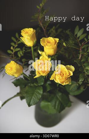 Ein sehr schönes Bouquet aus gelben Rosen steht in einer grünen Vase und zwei Gläsern Rotwein. Romantischer Abend. Schriftzug Happy Day Stockfoto