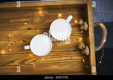 Zwei Tassen Cappuccino stehen auf einem Holztablett mit Lichtern Stockfoto