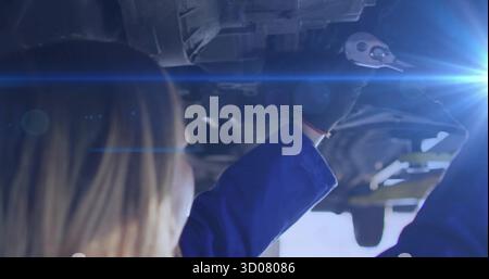 Mechaniker mit Handschuhen und Steckschlüssel unter angehobenem Fahrzeug in der Werkstatt unter Arbeitsscheinwerfer, Kopierraum Stockfoto