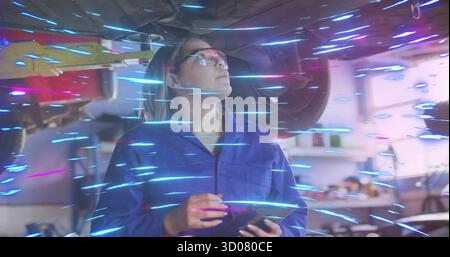 Asiatischer Mechaniker, der Overall trägt und das Laufwerk in der Werkstatt mit Tablet überprüft Stockfoto