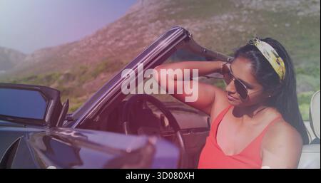 Frau in roter Spitze, die Haare in Cabrio auf Bergstraße fixiert, mit Sonnenbrille, Stirnband, Kopierraum Stockfoto