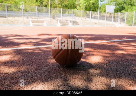 Ein Basketball, der sich an einem klaren, sonnigen Tag auf einem Sportplatz im Freien bei hellem Sonnenlicht ausruhen lässt und perfekt zum Spielen oder Üben geeignet ist Stockfoto