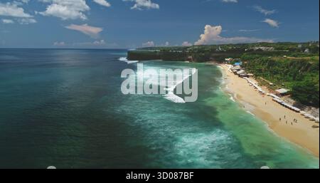 Atemberaubender Blick aus der Vogelperspektive auf Dreamland Beach in Bali, Indonesien, mit lebhaftem türkisfarbenem Wasser, sanften Wellen auf weißem Sand und üppigen grünen Klippen unter einem hellblauen Himmel Stockfoto