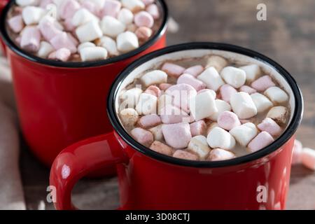 Heißes Schokoladengetränk mit Marshmallows in rotem Becher auf Holztisch Stockfoto