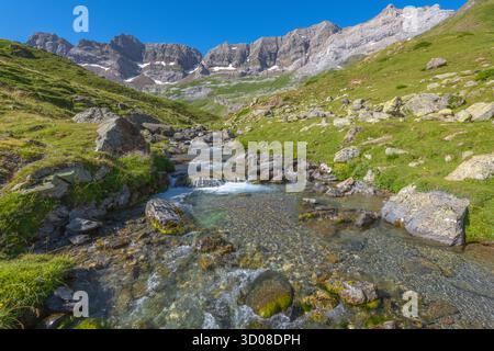 Das Estaubè-Tal in den französischen Pyrenäen, imposanter Bergkessel mit einem hohen, scharfen Kamm. Almweide mit einem kleinen Bergbach, der hinunterstürzt. Stockfoto