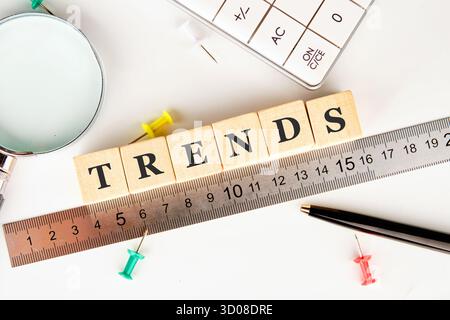 Farbenfrohe Buchstabenblöcke beschreiben Trends auf einem Lineal, umgeben von einer Lupe, Stecknadeln und einem Taschenrechner, die einen dynamischen Arbeitsbereich für einen darstellen Stockfoto