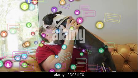 Mann in rotem Hemd, der schwarz-weißen Hund auf der Couch zu Hause umarmt, mit schwebenden Avataren, Chat-Blasen Stockfoto