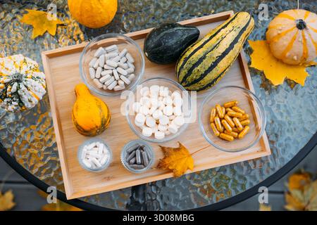 Flatlay von Herbstkürzeln und verschiedenen Beilagen in Glasschalen, die auf einem Holztablett über Herbstlaub angeordnet sind. Funktionelle Ernährung in der Natur Stockfoto