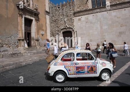 Touristen posieren für Fotos neben einem klassischen Fiat 500 in Taormina, Sizilien, Italien Stockfoto