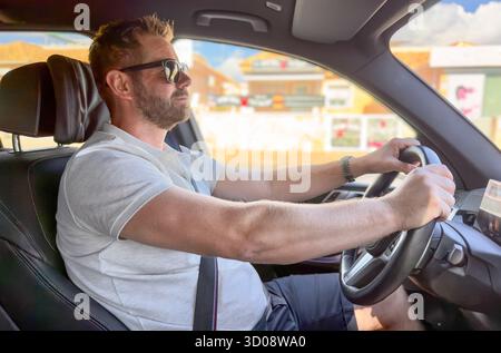 Junger bärtiger Mann mit Sonnenbrille, der sein Auto fährt. Reisekonzept. Stockfoto